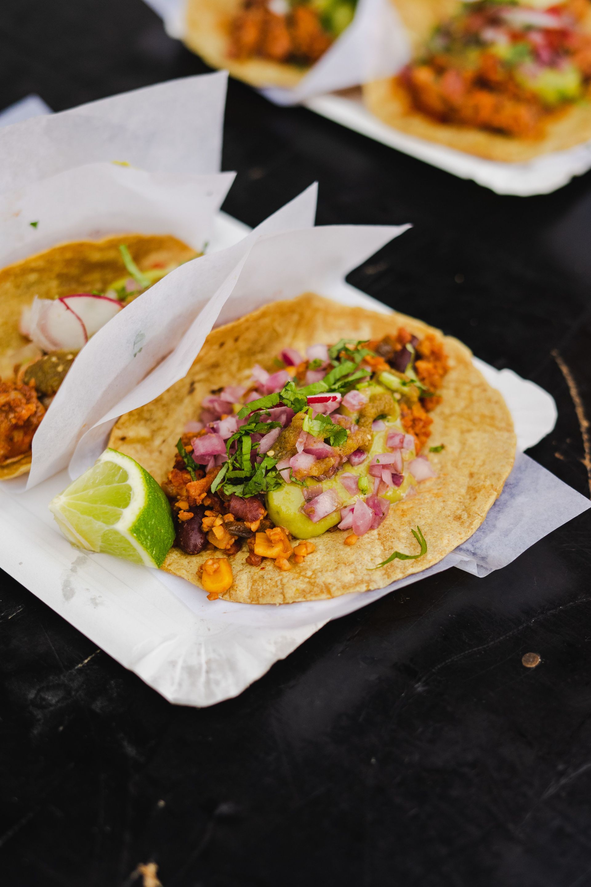 Authentic Mexican tacos topped with onions, cilantro, and guacamole served with a lime wedge.