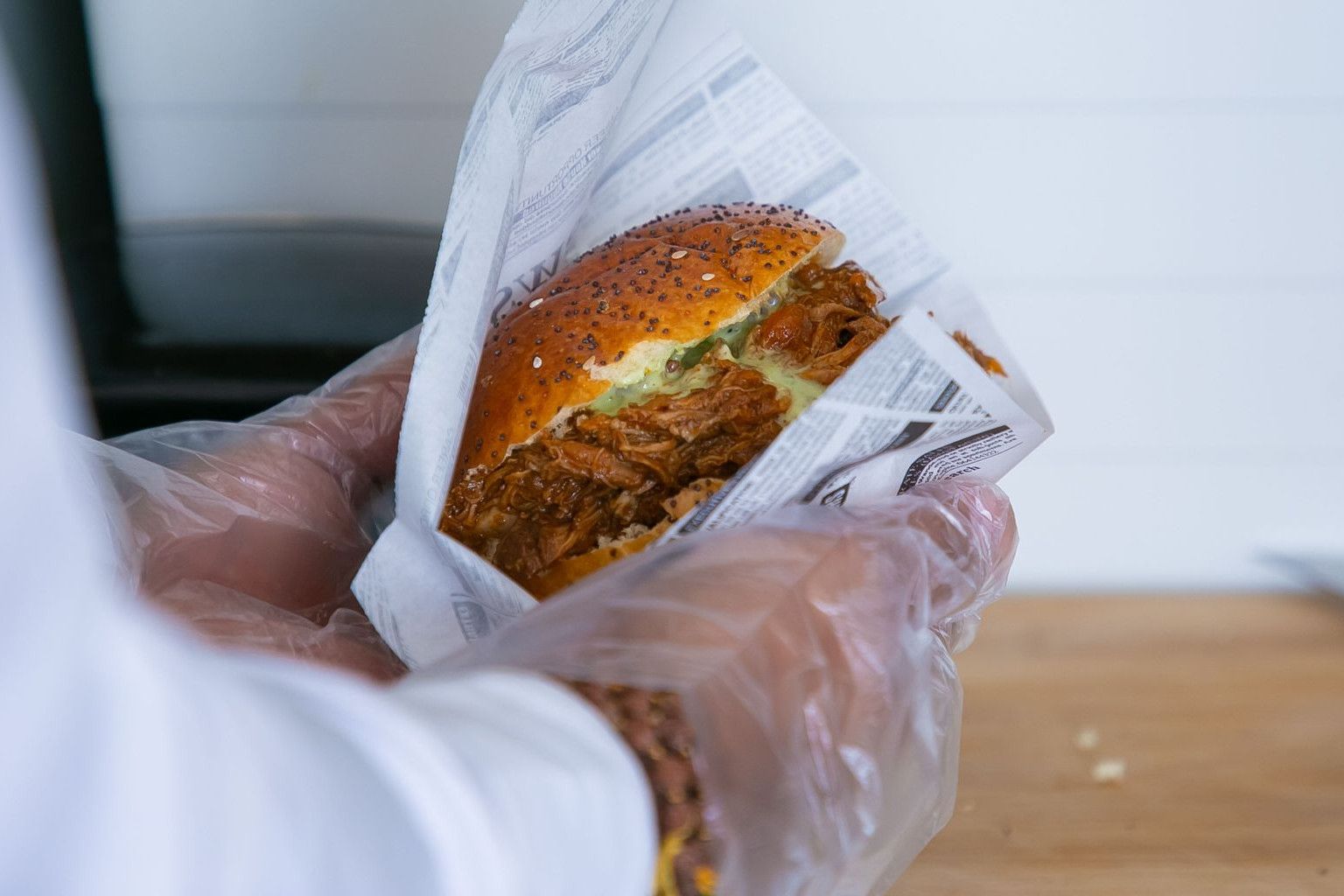 Crop anonymous male seller preparing order of burger with fried pork and bun with sesame